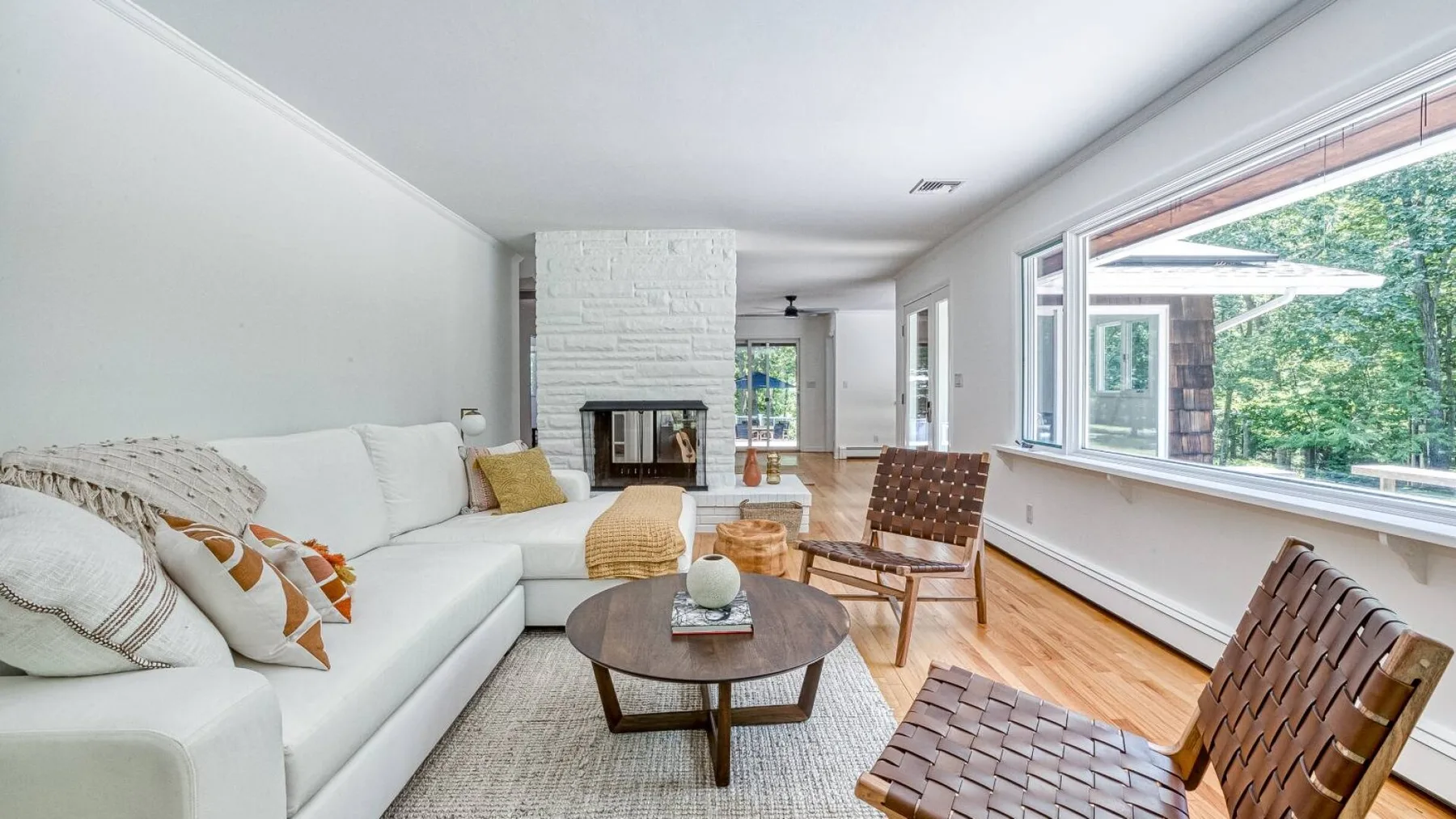A bright living room with white seating, a coffee table, and large windows.