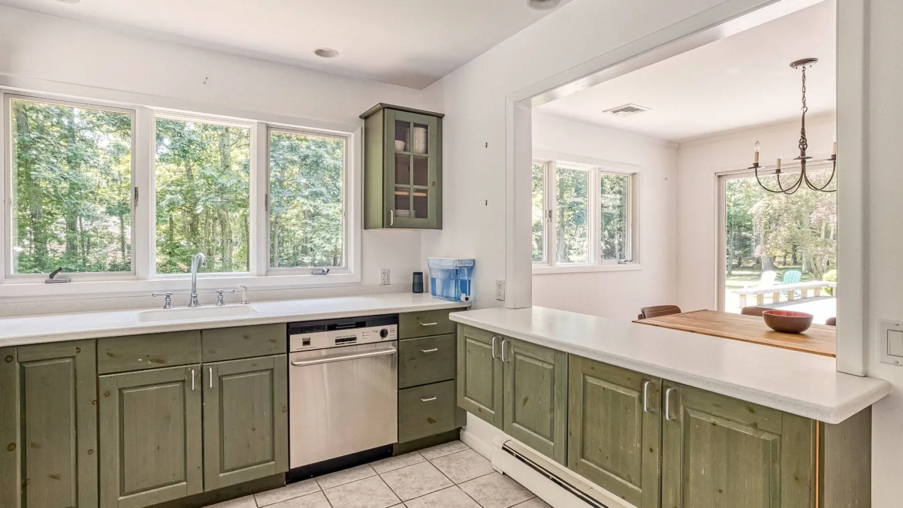 A bright kitchen with green cabinets, white countertops, and large windows.