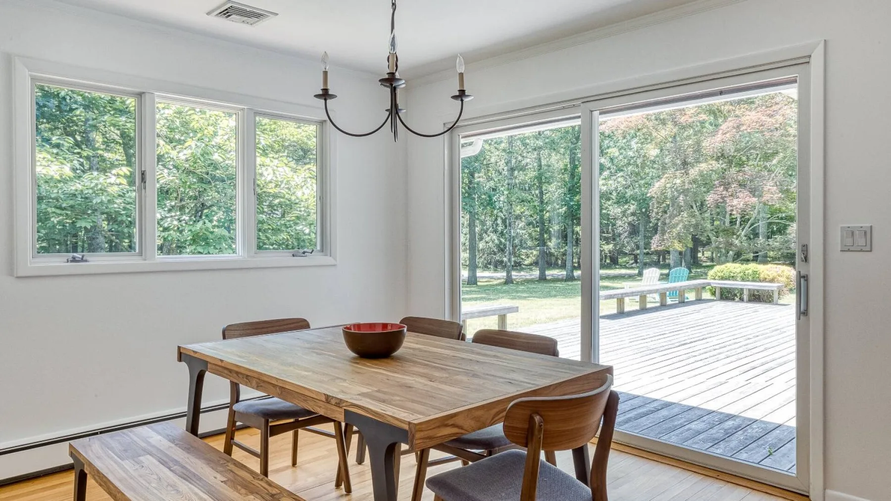 A dining area with a wooden table beside large windows opening onto a deck.