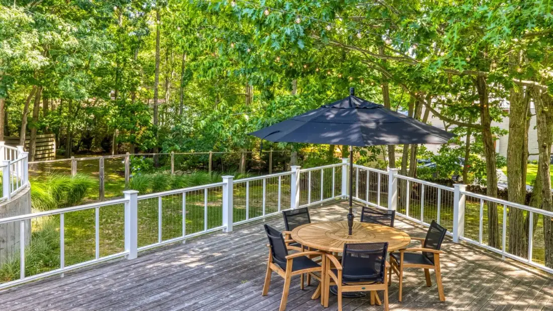 A deck with a round dining table and seating beneath a large umbrella.