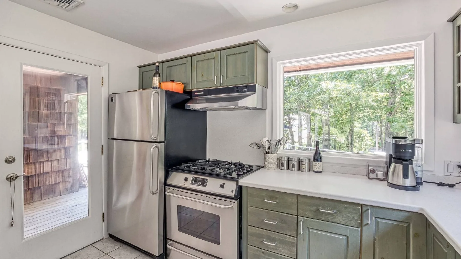 A kitchen with a stainless-steel refrigerator, stove, and wide window overlooking trees.