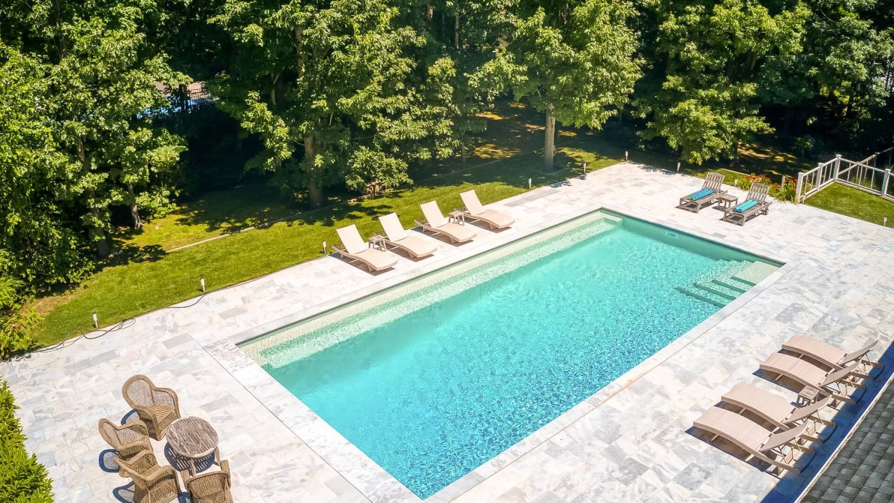 An outdoor swimming pool is surrounded by a paved deck and lounge seating.