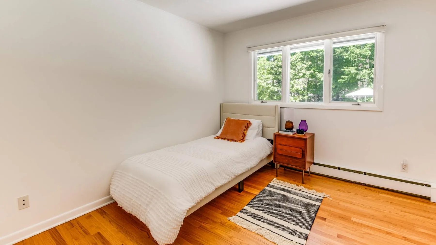 A small bedroom with a single bed, a bedside table, and a window.