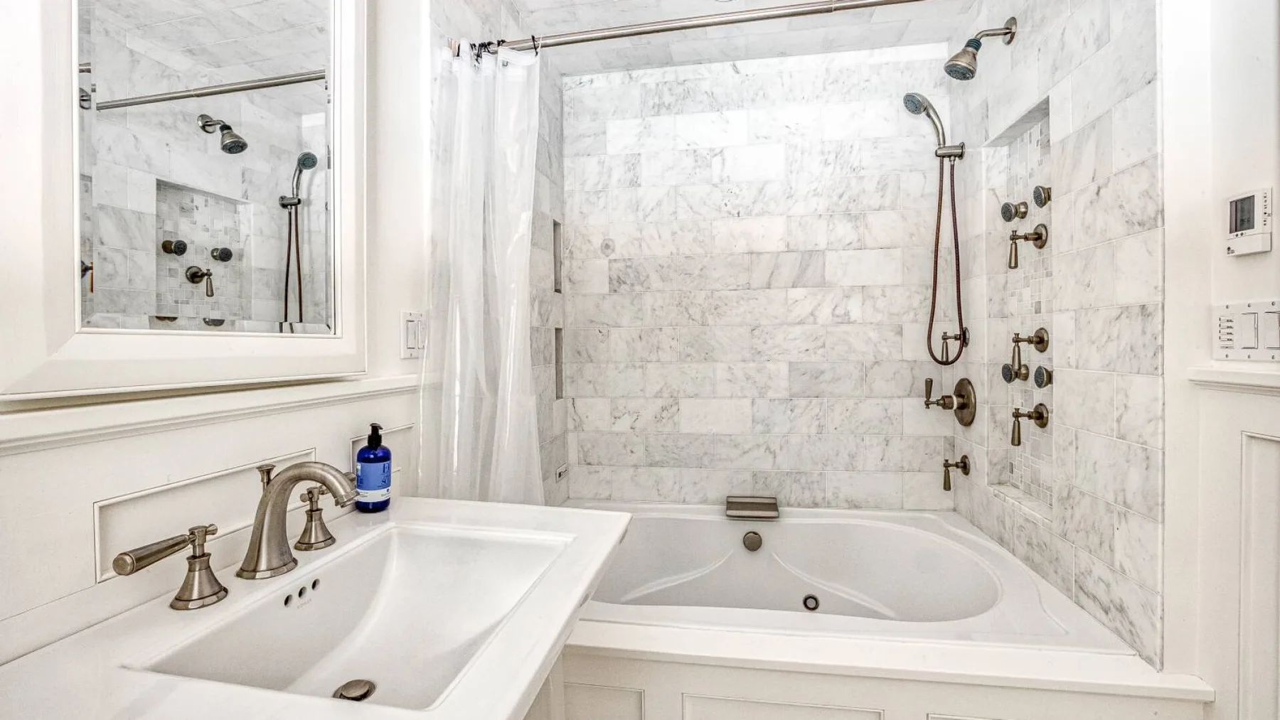 A marble bathroom features a sink and a large bathtub with shower fixtures.