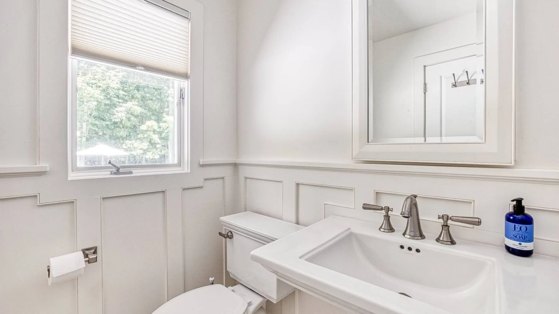 A bright bathroom with a wide sink, wall mirror, and window.
