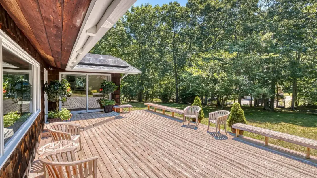 A wooden deck with outdoor seating overlooks a wooded yard.