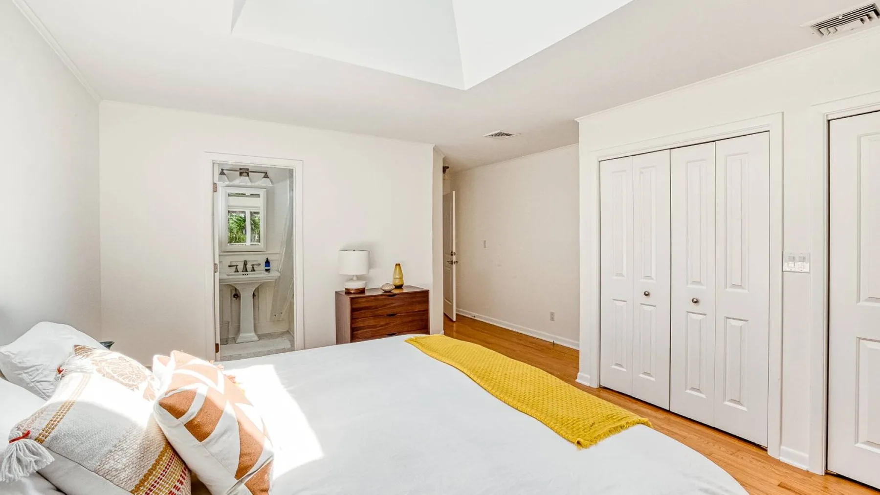 A bright bedroom with a bed, a yellow throw, and white closet doors.