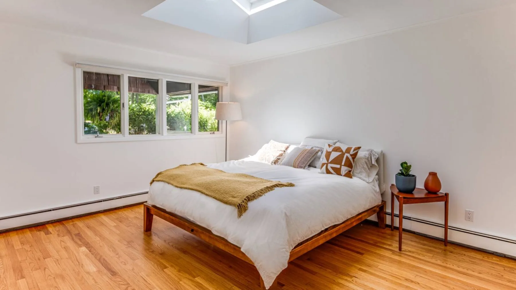 A bright bedroom with a neatly made bed and a wide window overlooking greenery.