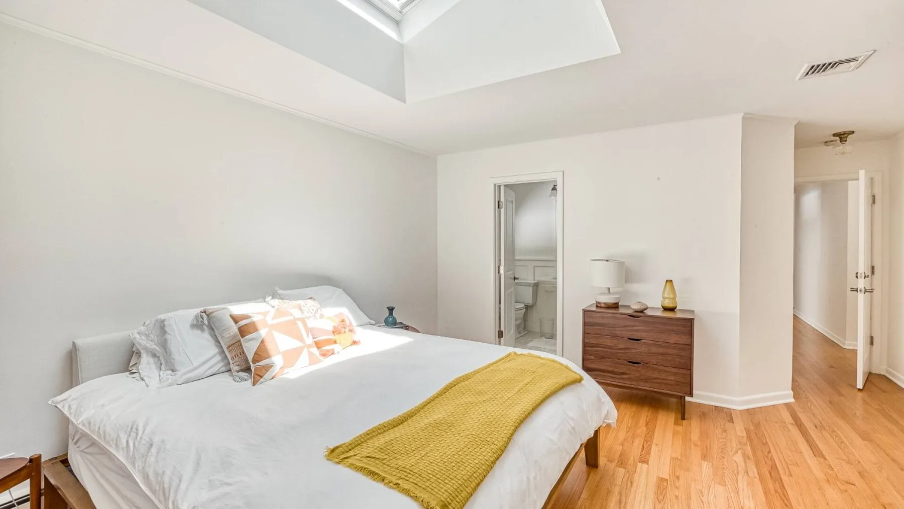 A bright bedroom with a bed, wooden dresser, and doorway to a bathroom.