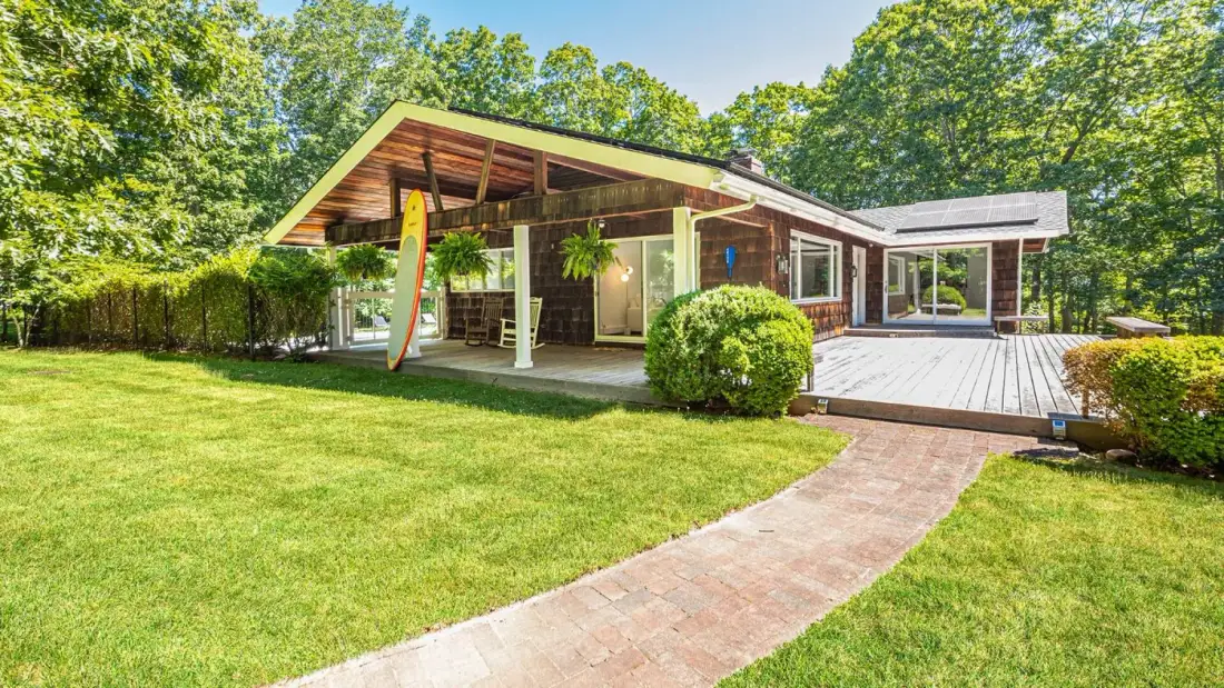 A modern house opens onto a broad wooden deck beside a green lawn.