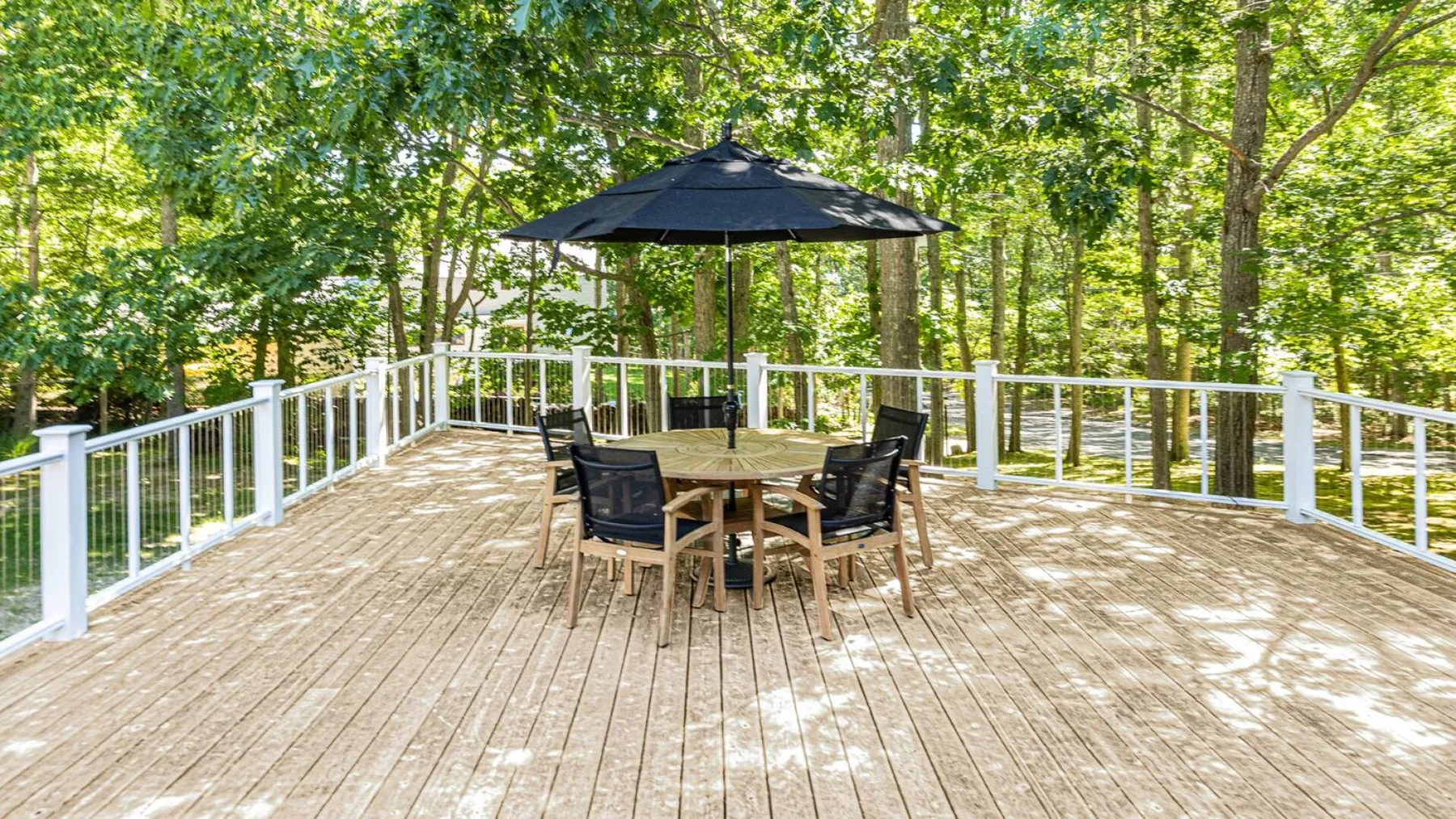 An outdoor deck with a dining table and umbrella, surrounded by trees.
