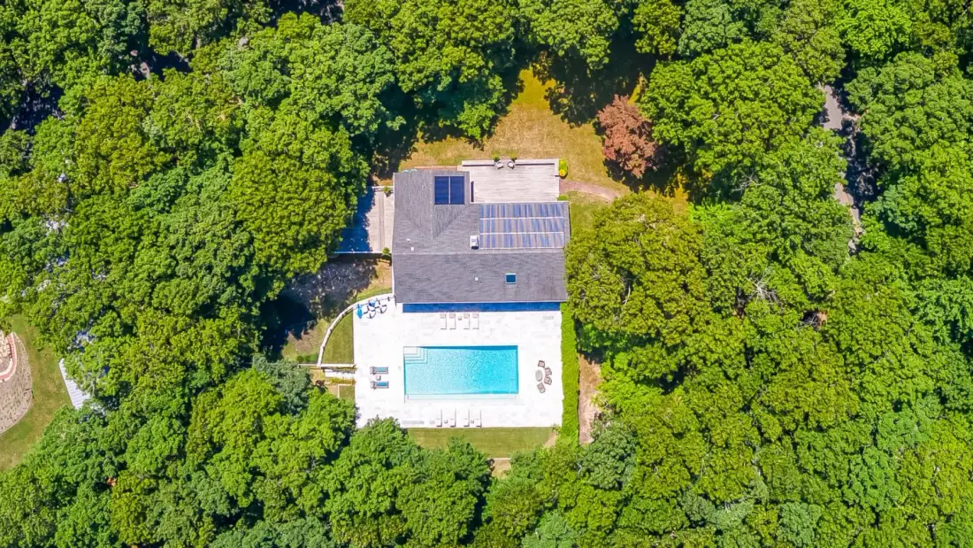 Aerial view of a house and swimming pool surrounded by dense trees.