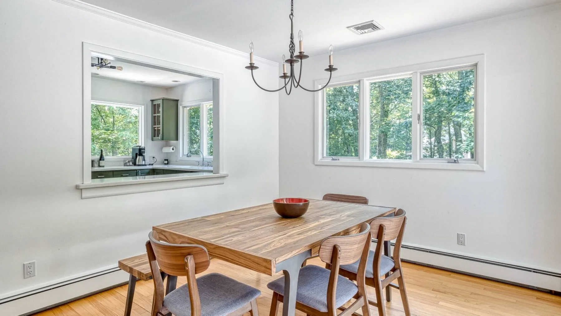 A bright dining area has a wooden table and windows overlooking trees.