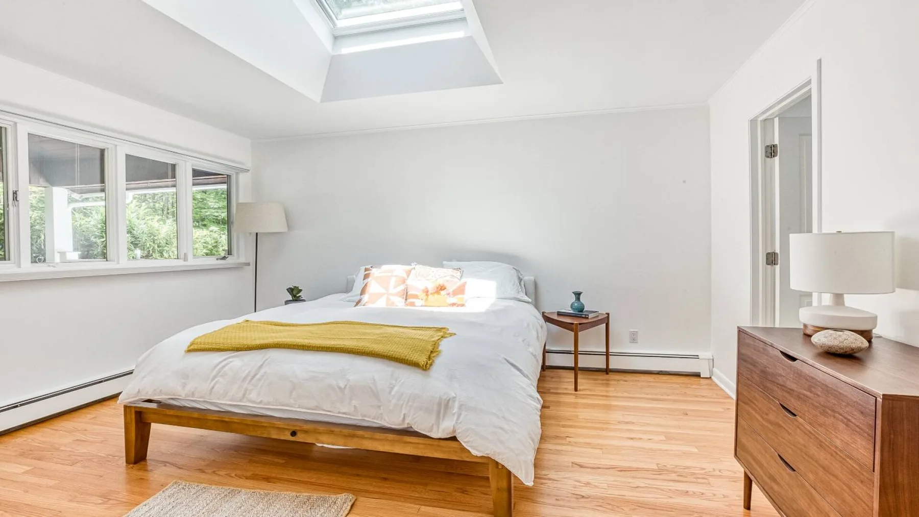 A bright bedroom with a bed beneath a skylight and windows along one wall.