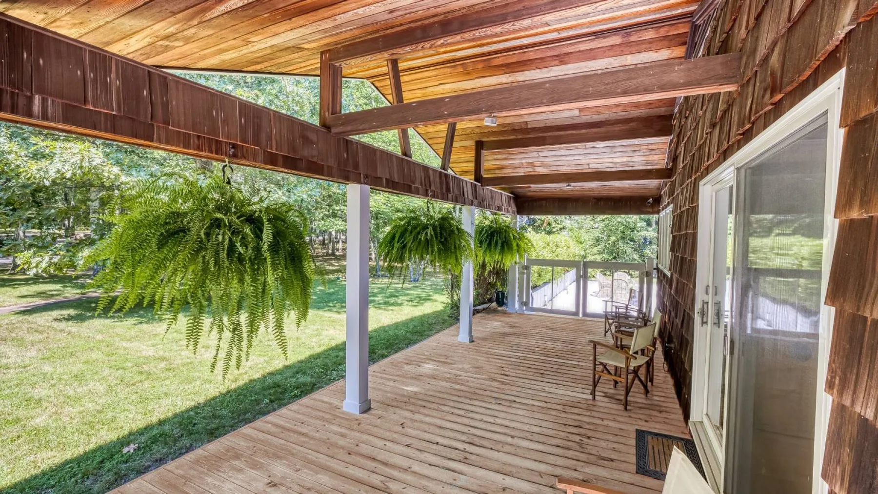 A covered wooden deck with seating overlooks a grassy yard.
