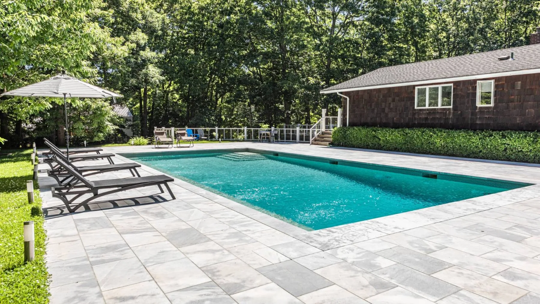 An outdoor swimming pool is surrounded by a paved patio and lounge seating.