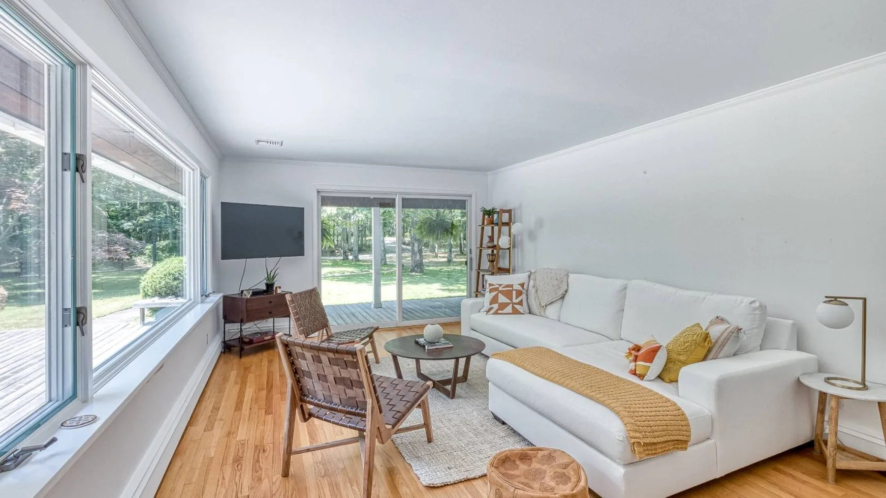 A bright living room with a white sofa and large windows overlooking greenery.