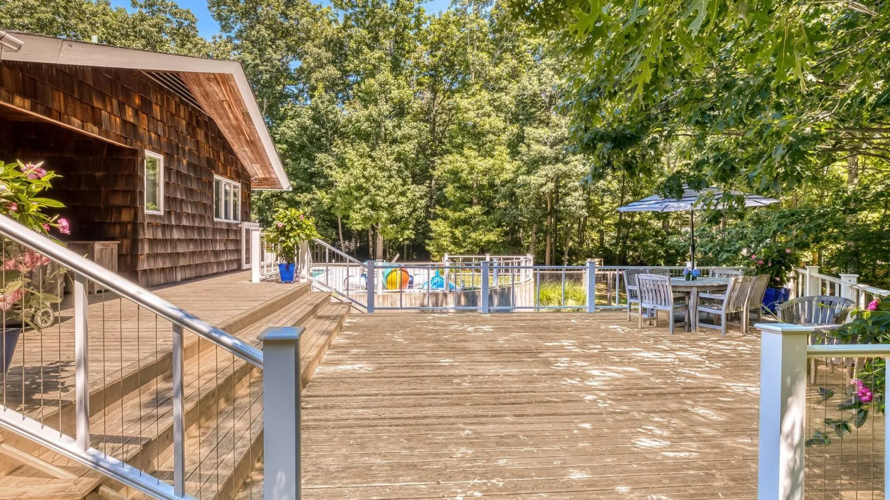An outdoor wooden deck beside a cabin, with railings, seating, and trees.
