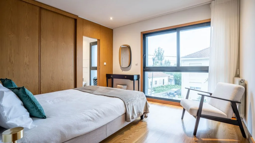 A bedroom with a bed, a chair, and a large window.