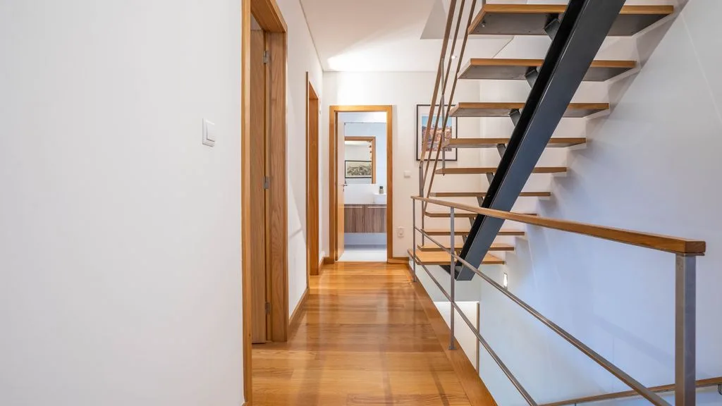 A bright interior hallway with a wooden floor and open staircase.