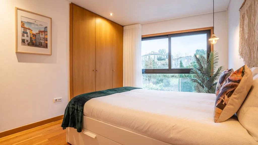 A bedroom with a neatly made bed, wooden wardrobe, and large window.