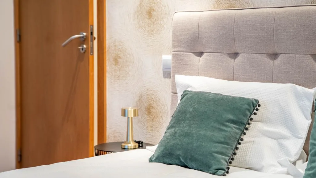 A bedroom with a bed, green cushion, and wooden door.
