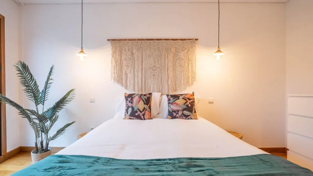 A bedroom with a bed, patterned pillows, and pendant lights.