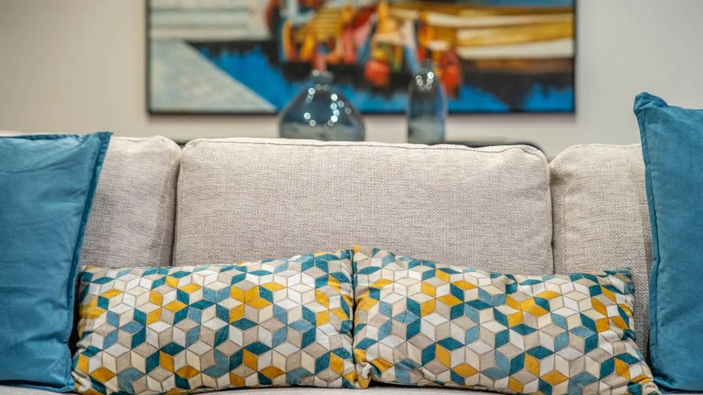 A living room seating area with patterned cushions and colorful artwork above the sofa.