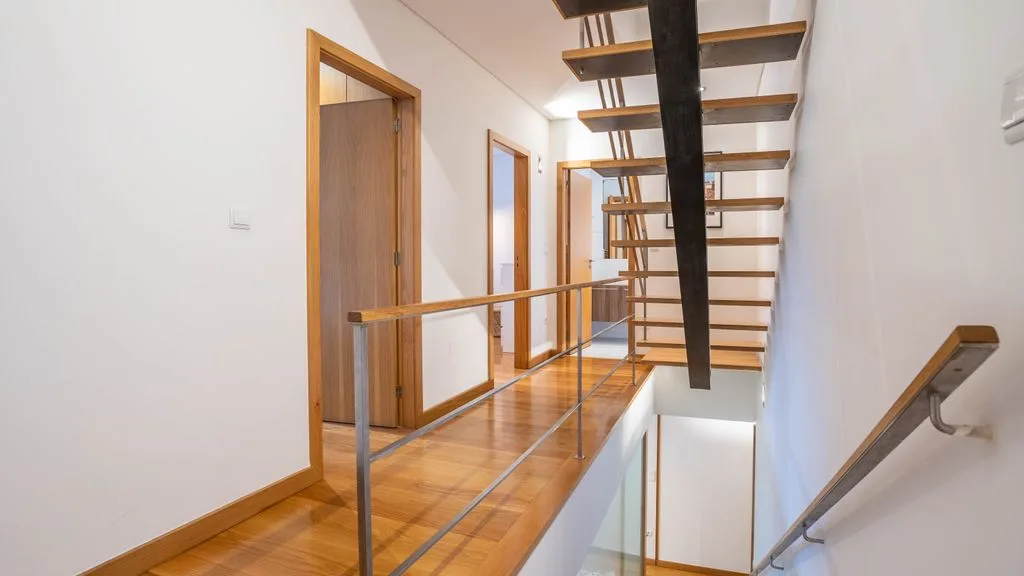 A bright hallway with wooden flooring and an open staircase.