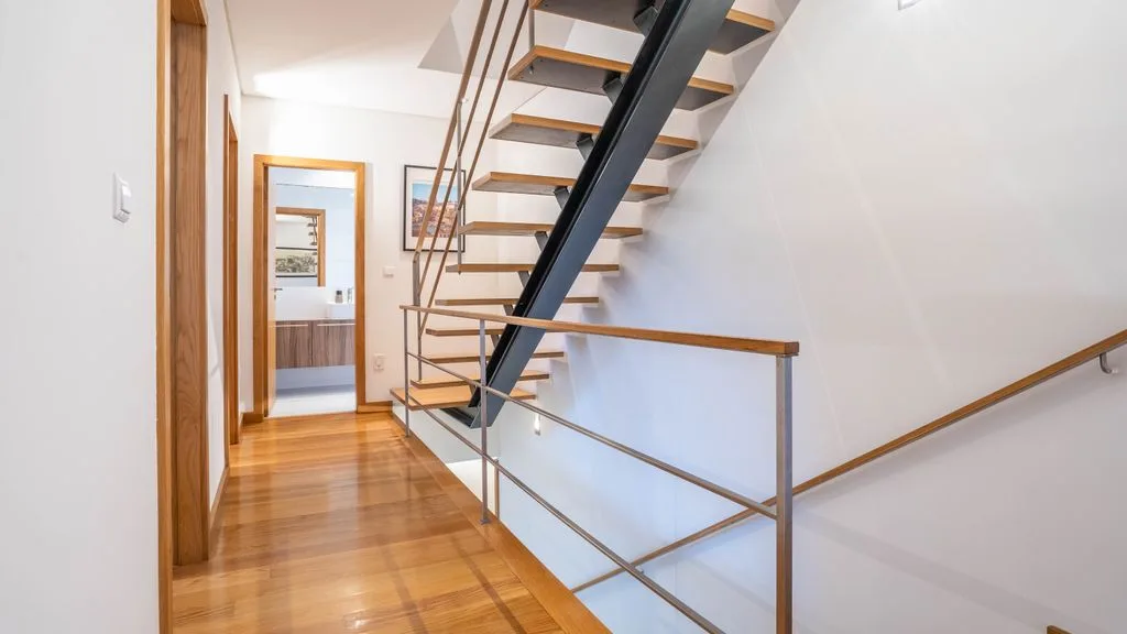 A bright interior hallway with wooden flooring and an open staircase.