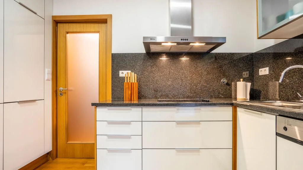 A modern kitchen with white cabinets, a dark backsplash, and a stainless steel range hood.