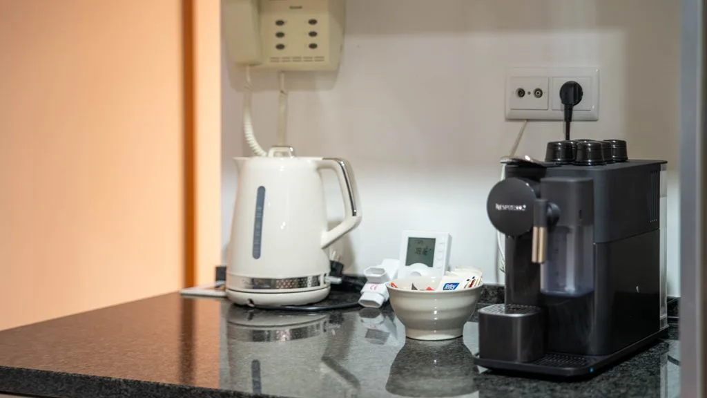 A kitchen counter holds a kettle, coffee machine, and small bowl.