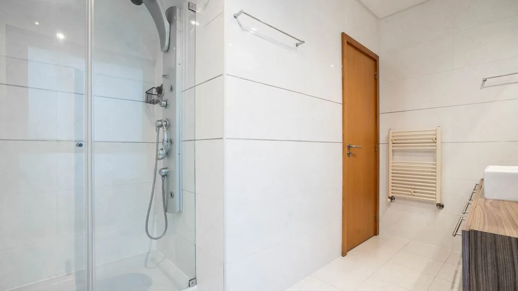 A bright bathroom with a glass shower and a wooden door.