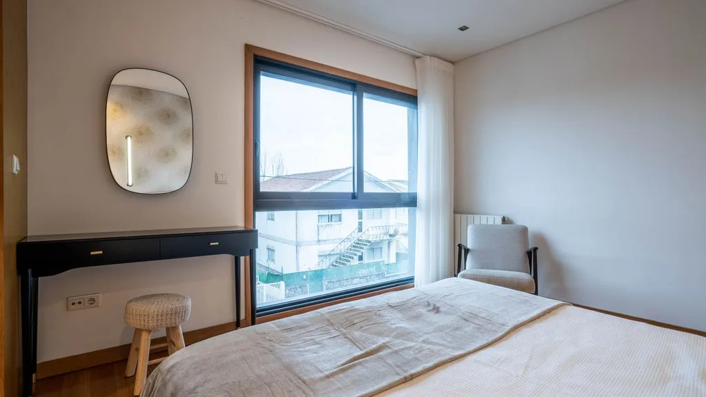 A bedroom with a large window, a bed, and a small desk.