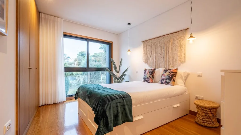 A bedroom with a bed beside a large window and curtains.