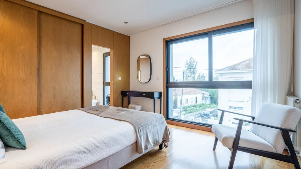 A bedroom with a bed, wooden wardrobe, and large window.