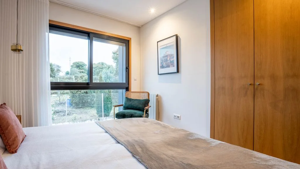 A bedroom with a bed, an armchair, and a large window.