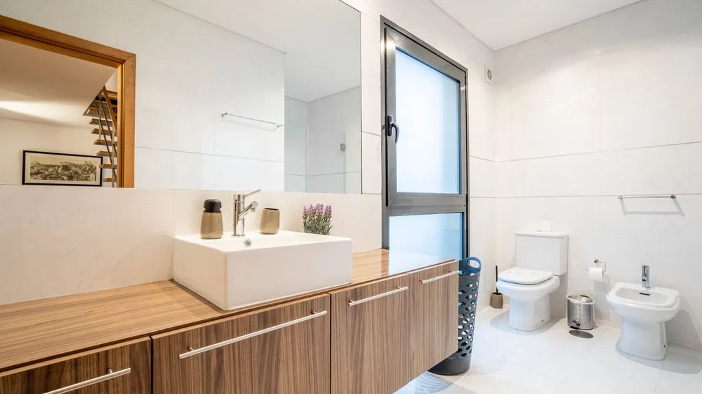 A bathroom with a wide vanity, mirror, toilet, and sink.