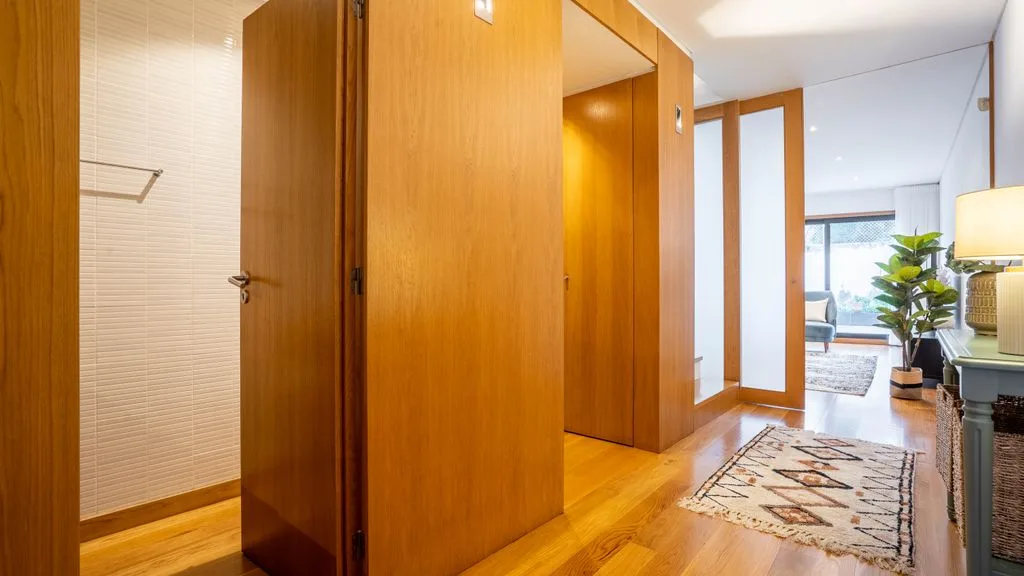 A bright hallway with wooden doors and a patterned rug.