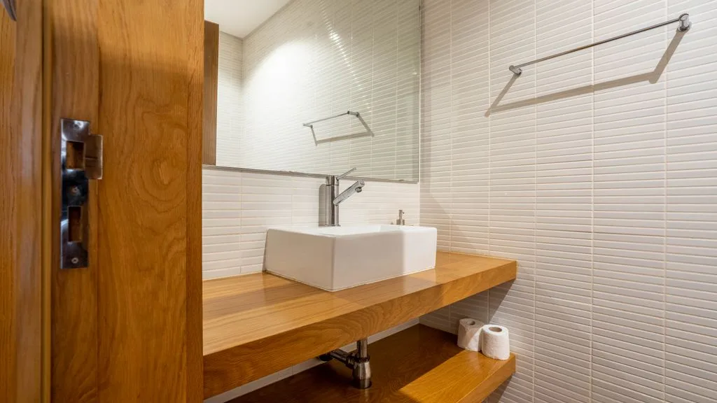 A modern bathroom with a white vessel sink on a wooden counter.