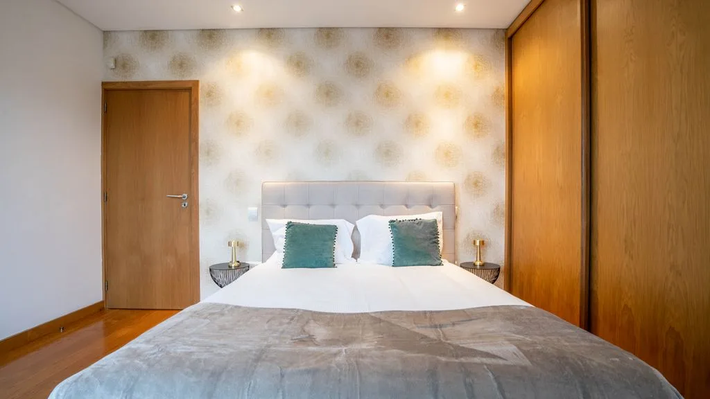 A bedroom with a bed, patterned wallpaper, and wooden doors.