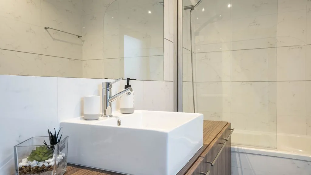 A bathroom vanity with a white vessel sink and a glass shower.