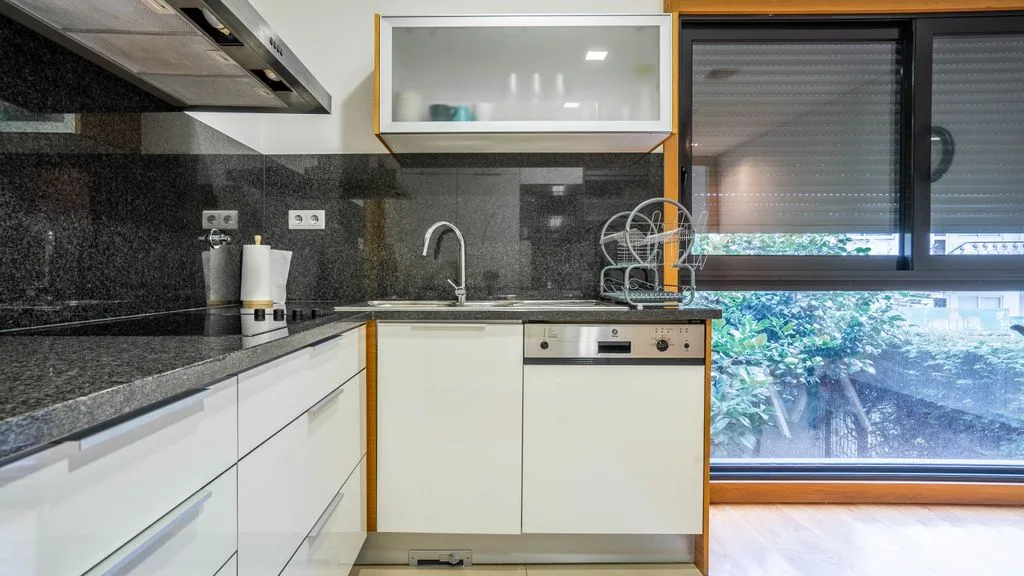 A modern kitchen with white cabinets, dark countertops, and a sink.