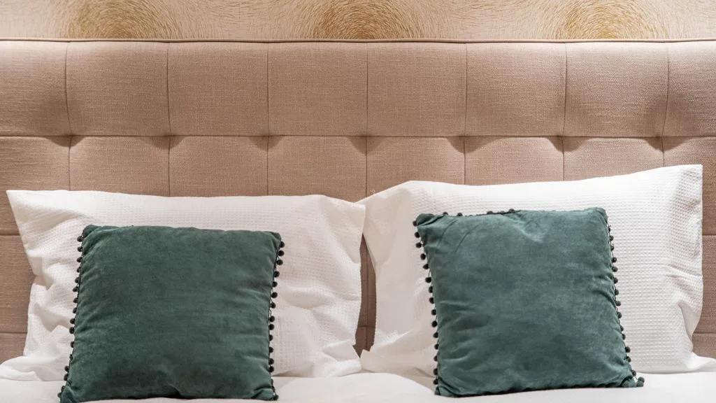 A bedroom scene with a tufted headboard and green accent pillows.