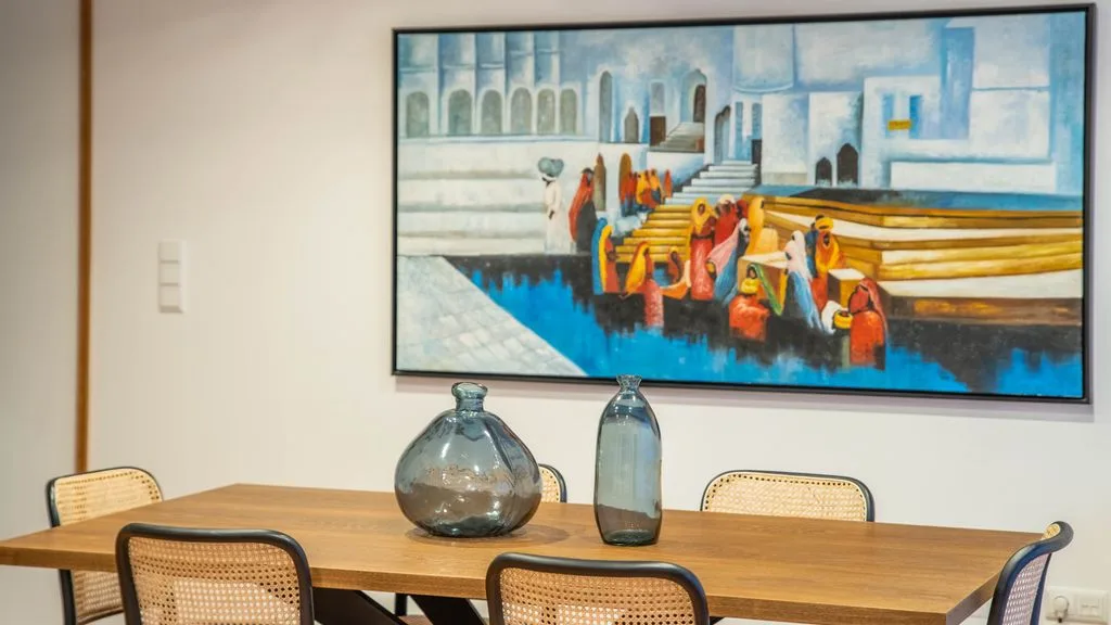 A dining area with a wooden table beneath a colorful framed painting.