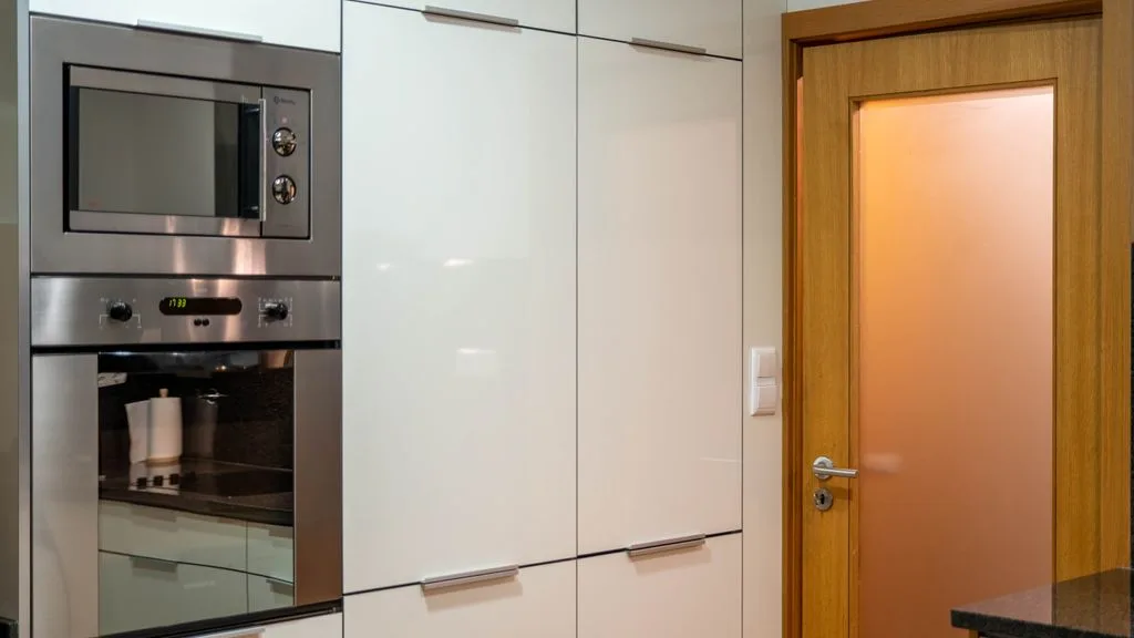 A modern kitchen with built-in appliances and a wooden door.