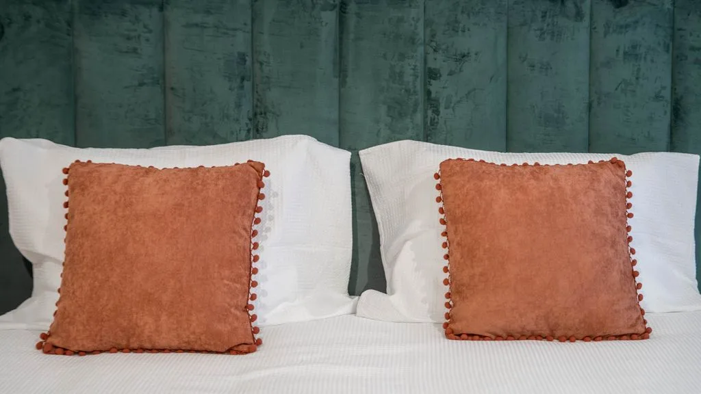 A bed with white pillows and rust-colored accent cushions against a green wall.