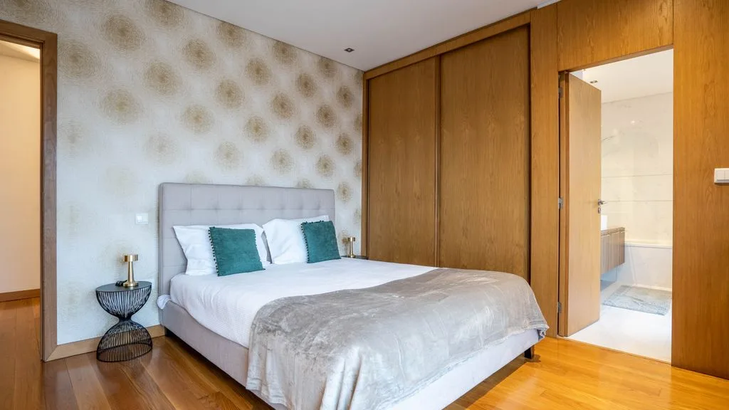 Un dormitorio con una cama junto a un armario de madera y una puerta abierta al baño.