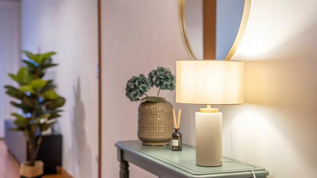 A table lamp and decorative vase sit on a console table beside a mirror.