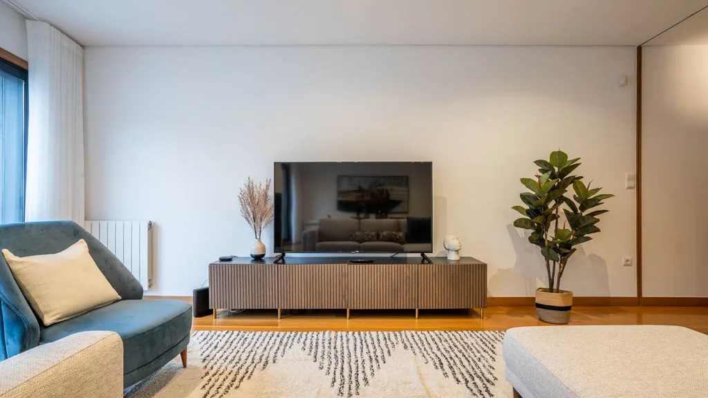 A living room with a television on a media console and seating beside a window.